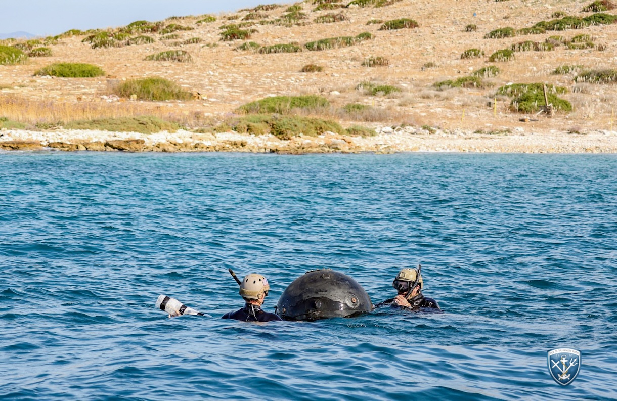 Δύο δύτες με καταδυτικό εξοπλισμό και κράνη δίπλα σε θαλάσσια νάρκη στο νερό