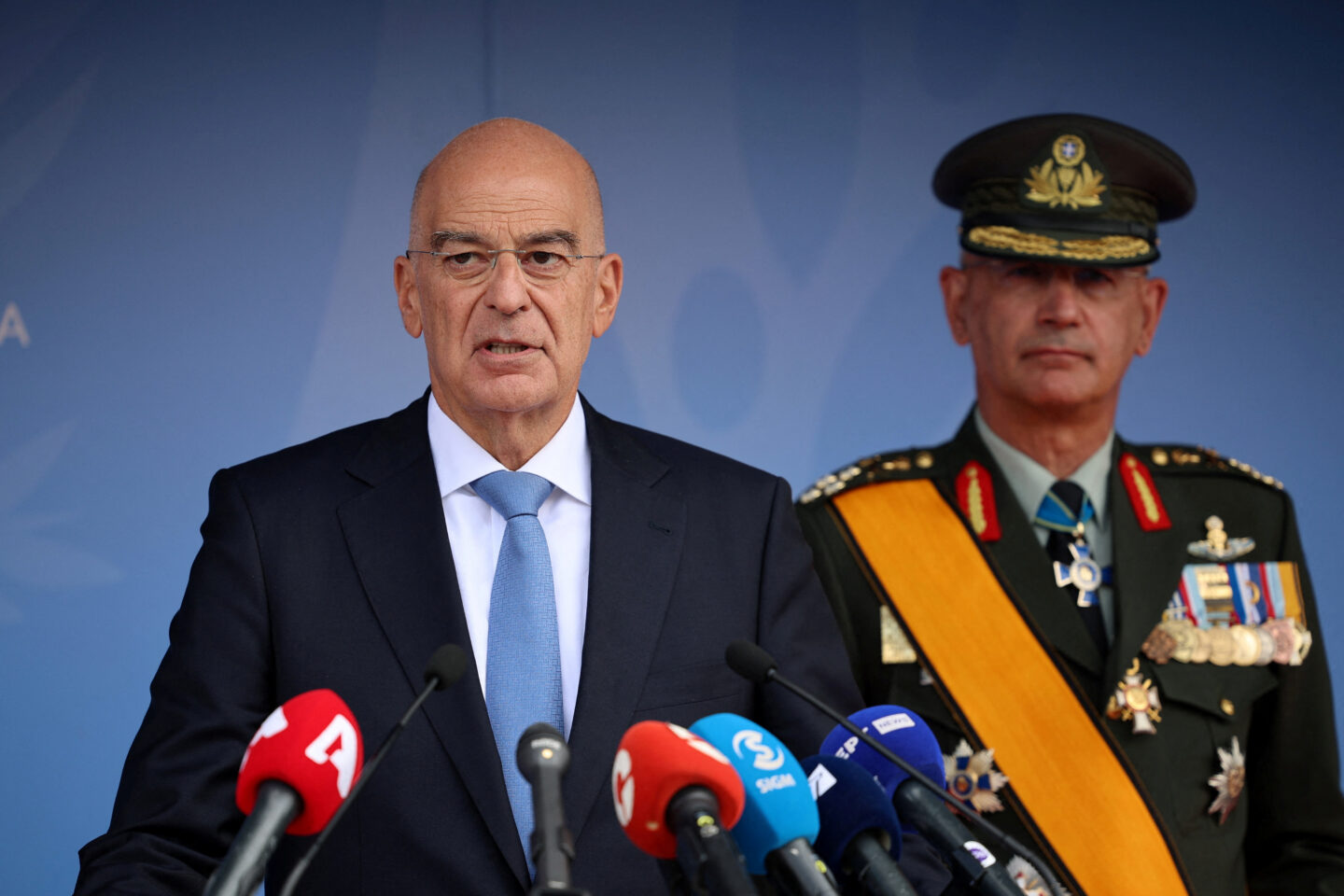 Ο Νίκος Δένδιας κάνει δηλώσεις μπροστά σε μικρόφωνα με τον Α/ΓΕΕΘΑ Χούπη στο βάθος
